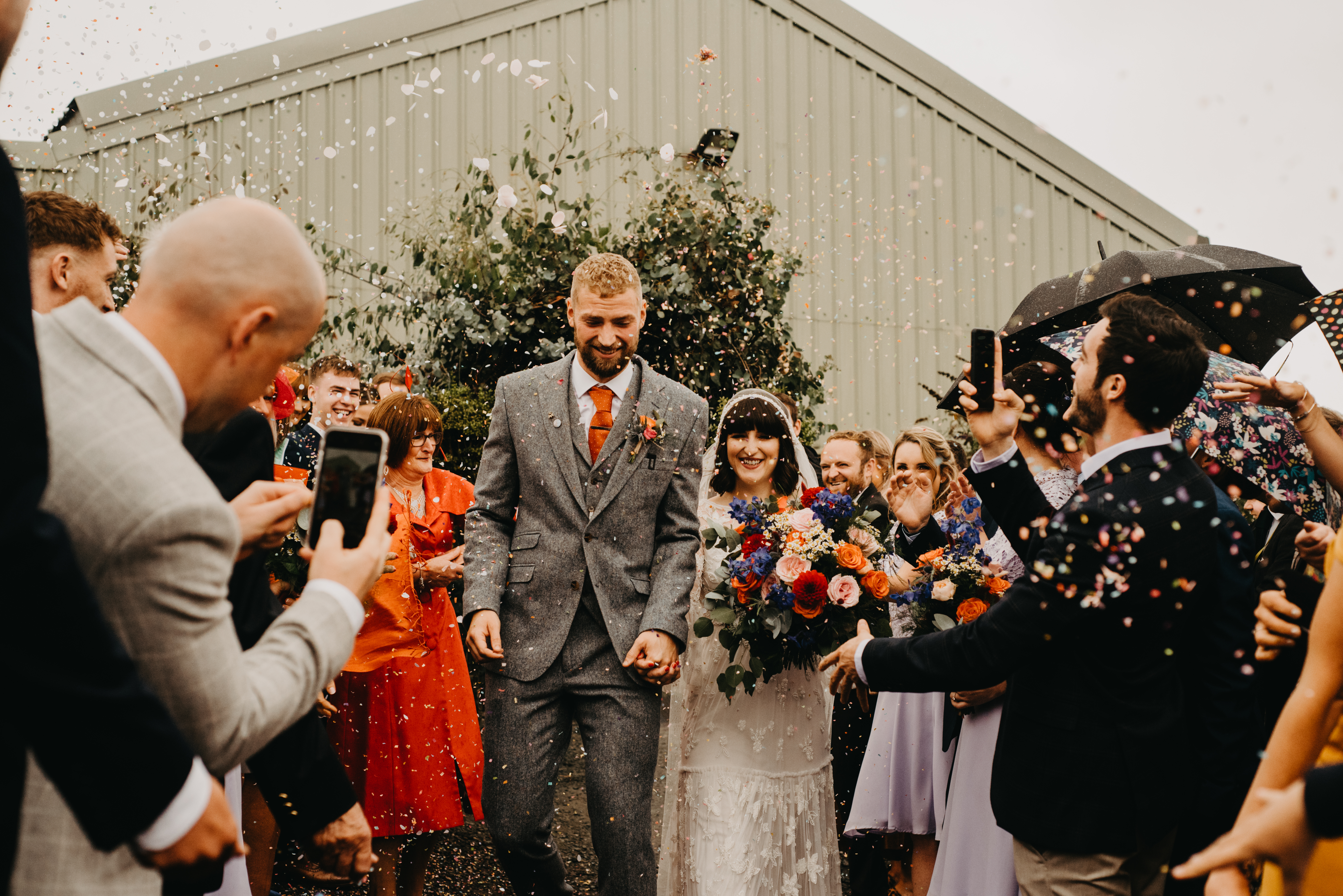 Bride and groom walks while guests throws confetti over them
